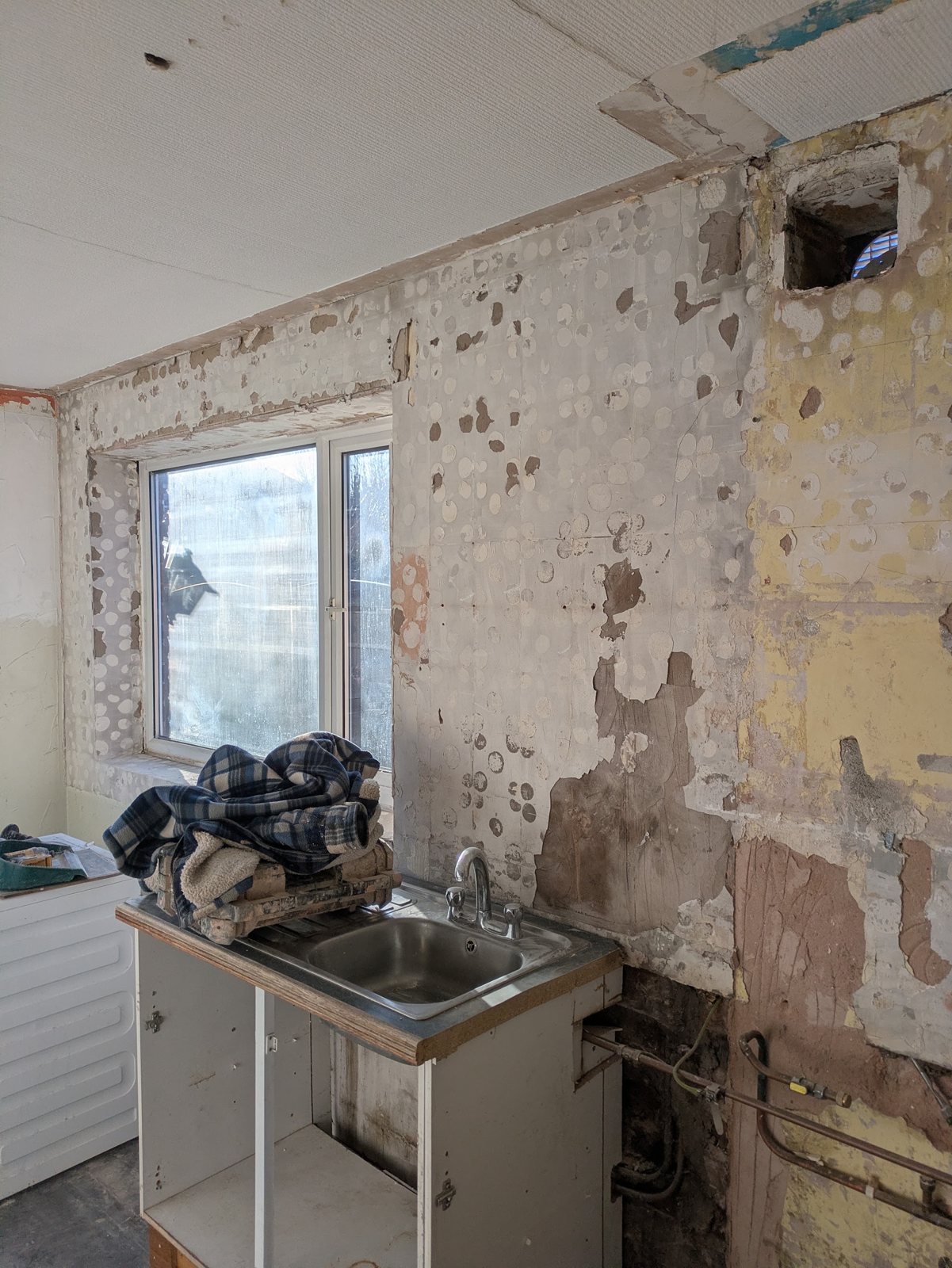 A kitchen wall stripped back to old, patchy plaster around the window before work starts