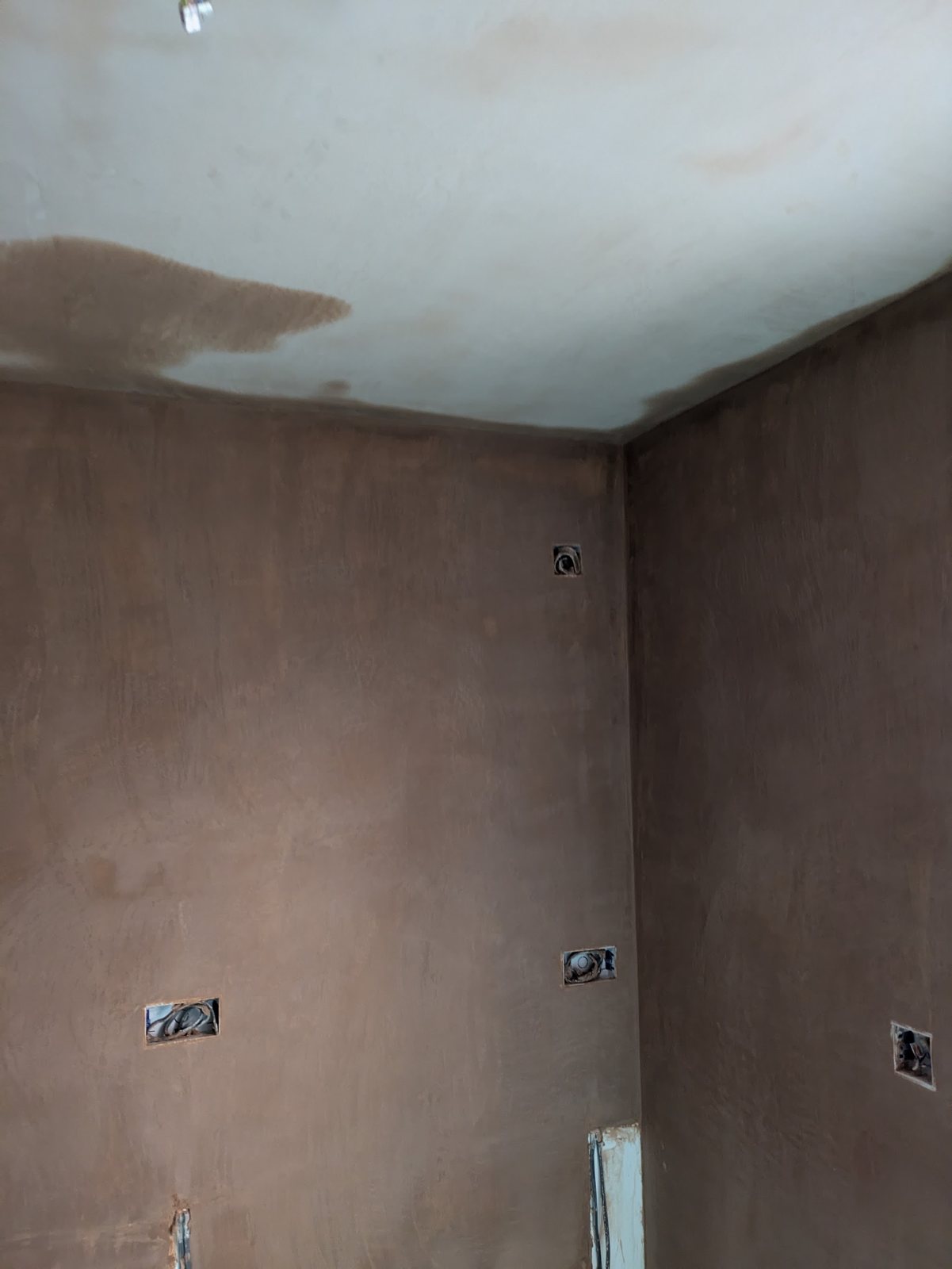 A room with walls and ceiling freshly skimmed, the plaster still dark and drying